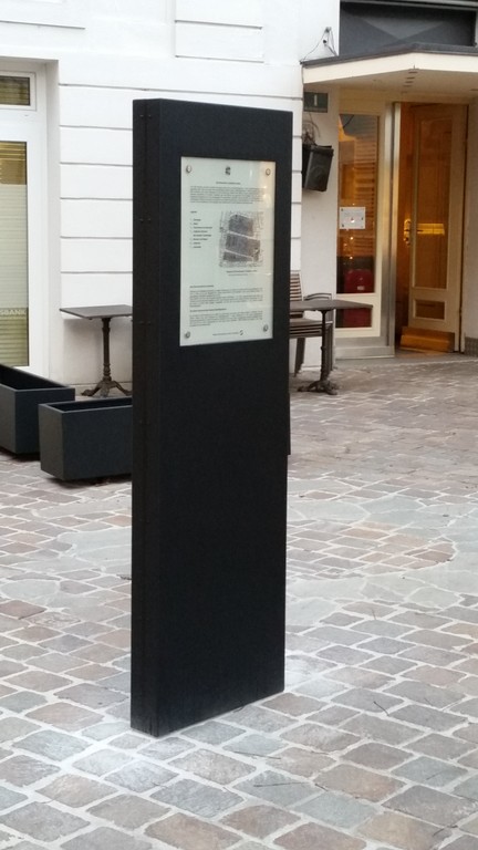 Rückseite der Stele - mit dem Eingang in das Haus Allerheiligenplatz 1 (einst Synagoge, heute Café Witetschka) im Hintergrund